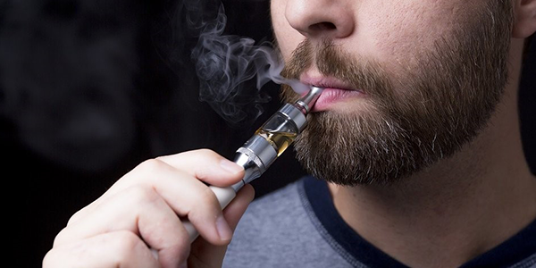 White man with beard vaping from an e-cigarette
