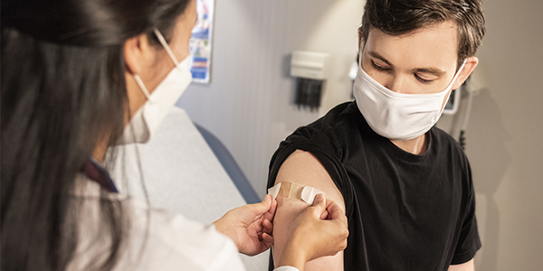 Young man receiving a band aid over a vaccine from a female doctor