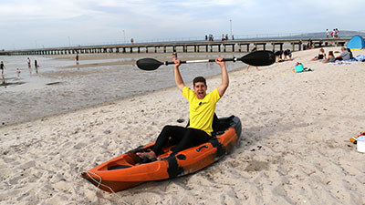 A guy in a kayak at the beach holding the paddle up above his head