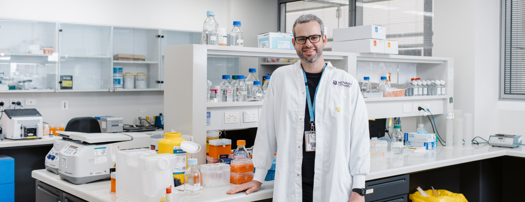 Male scientist in white coat, smiling, in laboratory